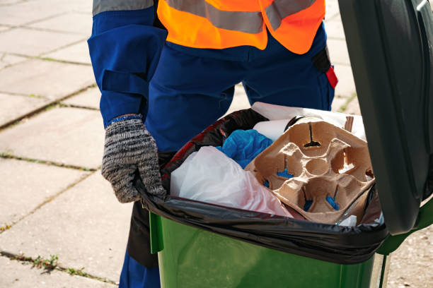 Male janitor in uniform cleans a trash can in the street close up